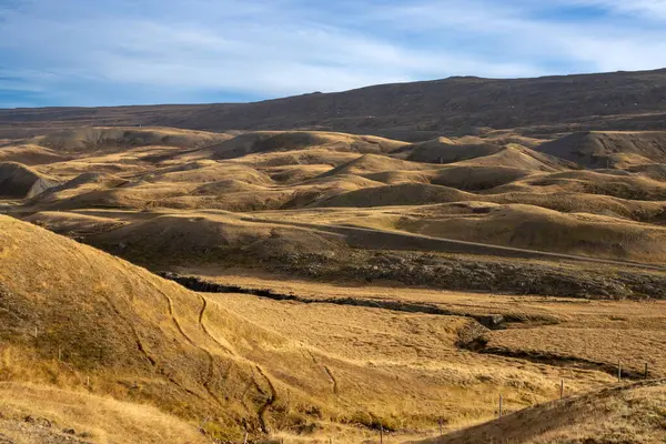 Küçük tepelerin dalgaları, çimenler, yosunlar ve yosunlarla kaplıdır. Sonbaharda beyaz bulutlu mavi gökyüzü. Jokuldal, Doğu İzlanda.