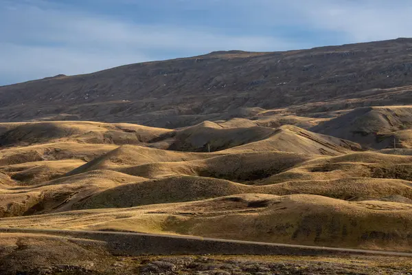 Küçük tepelerin dalgaları, çimenler, yosunlar ve yosunlarla kaplıdır. Sonbaharda beyaz bulutlu mavi gökyüzü. Jokuldal, Doğu İzlanda.