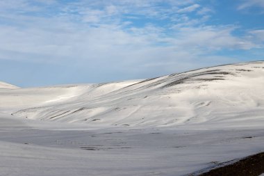 Mavi gökyüzü ve beyaz bulutlarla güzel bir sonbahar günü. Dalgalar ve küçük tepelerle kaplanmış taze kar. Kuzey-Doğu İzlanda.