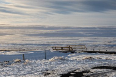 Sonbahar karının ince tabakası. Her şey örtülü ve beyaz, ufukta bulutlu gökyüzü görünüyor. Küçük köprü. Bardardalsvegur Eystri, Kuzey İzlanda.