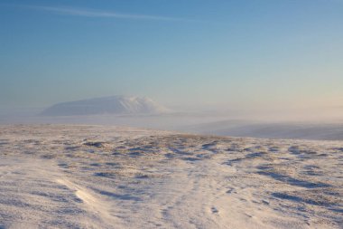Karla kaplı bir tepedeki arazi. Ufukta dağ görünüyor. Mavi gökyüzü ve ışık bulutları. Altın saat. Fossholl-Godafoss, Kuzey İzlanda.