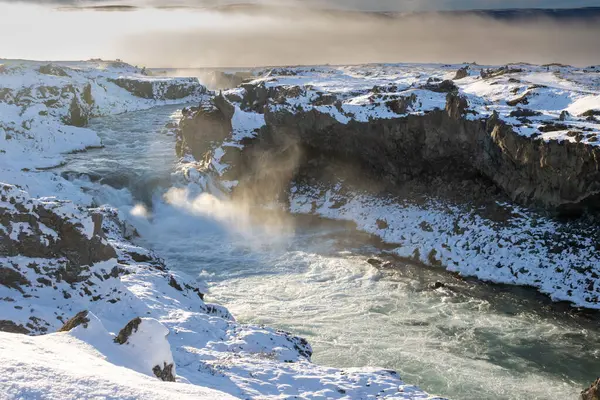 Part of the famous waterfall. Backlight of the winter sun. The air full of steam, spray and fog. Godafoss, North Iceland.
