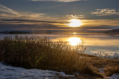 Sabahın erken saatlerinde kutup gündoğumunda. Karlı bir dağ ve bir fiyordun suyundaki yansıması. Mavi gökyüzü ve ışık bulutları. Güneş hala batıyor. Nordaustur, Kuzey-Batı İzlanda.