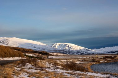 Dağlarla çevrili bir vadi. Çayırların arasında akan nehir sonbahar karının ince tabakasıyla kaplıydı. Bulutlu mavi gökyüzü. Vikurskard, Kuzey-Batı İzlanda.