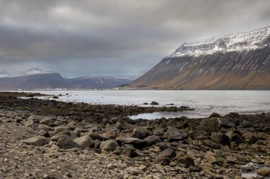 Westfjords bölgesinin vahşi kıyı şeridi. Atlantik Okyanusu 'nun sakin suları ve sonbaharda biraz karla görkemli dağlar. Bulutlu gökyüzü. Isafjordur Bölgesi, Kuzey-Batı İzlanda.