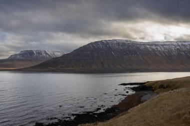 Westfjords bölgesinin vahşi kıyı şeridi. Atlantik Okyanusu 'nun sakin suları ve sonbaharda biraz karla görkemli dağlar. Bulutlu gökyüzü. Isafjordur Bölgesi, Kuzey-Batı İzlanda.