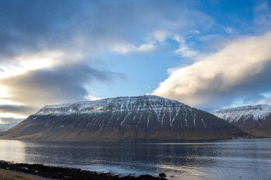 Bulutlu gökyüzü, fiyorttaki Atlantik Okyanusu 'nun sakin sularında yansıyor. Sonbaharda biraz kar yağan görkemli tepeler. Beyaz bulutlu mavi gökyüzü. Westfjords, İzlanda Bölgesi, ben güvenli Ürdün