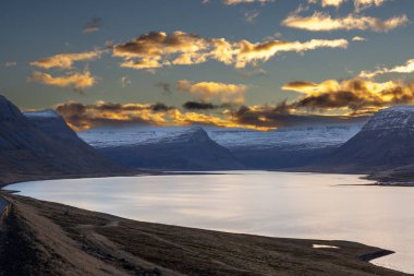 Dağlar karla kaplı. Gün batımında mavi gökyüzünde renkli bulutlar fiyorttaki Atlantik okyanusunun sakin suları. Westfjords, Isafjordur, İzlanda Bölgesi.