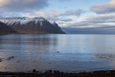 Bulutlu gökyüzü, fiyorttaki Atlantik Okyanusu 'nun sakin sularında yansıyor. Sonbaharda biraz kar yağan görkemli tepeler. Beyaz bulutlu mavi gökyüzü. Westfjords, İzlanda Bölgesi, ben güvenli Ürdün