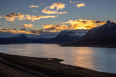 Dağlar karla kaplı. Gün batımında mavi gökyüzünde renkli bulutlar fiyorttaki Atlantik okyanusunun sakin suları. Westfjords, Isafjordur, İzlanda Bölgesi.
