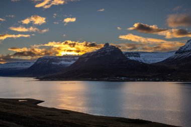 Dağlar karla kaplı. Gün batımında mavi gökyüzünde renkli bulutlar fiyorttaki Atlantik okyanusunun sakin suları. Westfjords, Isafjordur, İzlanda Bölgesi.
