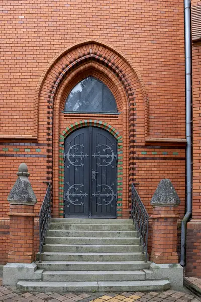 Side door to the building of a neo-gothic church of Visitation of Virgin Mary, made of orange bricks. Wide opened dark brown wooden gate. Postorna, Breclav, Moravia, Czech republic.