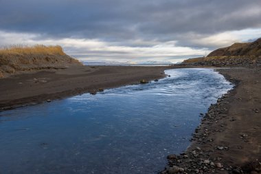 Nehrin kenarında okyanusa akan karanlık volkanik kum. Ufukta uçurumları, kar zirveleri olan dağlar. Isafjordur, Westfjords, İzlanda Bölgesi.