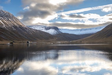 Mavi gökyüzü ve bulutlarla gün batımının başlangıcı. Fiyortta Atlantik Okyanusu 'nun Suyu. Sonbaharda biraz kar yağan görkemli tepeler. Westfjords, Isafjordur, İzlanda Bölgesi.