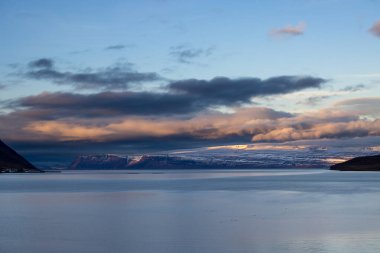 Dağlar karla kaplı. Gün batımında mavi gökyüzünde renkli bulutlar fiyorttaki Atlantik okyanusunun sakin suları. Westfjords, Isafjordur, İzlanda Bölgesi.