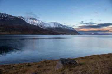 Dağlar karla kaplı. Gün batımında mavi gökyüzünde renkli bulutlar fiyorttaki Atlantik okyanusunun sakin suları. Westfjords, Isafjordur, İzlanda Bölgesi.