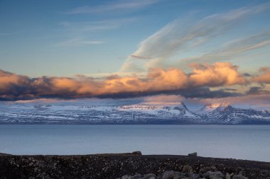 Dağlar karla kaplı. Gün batımında mavi gökyüzünde renkli bulutlar fiyorttaki Atlantik okyanusunun sakin suları. Westfjords, Isafjordur, İzlanda Bölgesi.