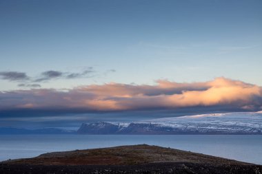 Mountains touched with snow. Colorful clouds on the blue sky during sunset Calm water of the Atlantic ocean in the fjord. Area of Westfjords, Isafjordur, Iceland. clipart