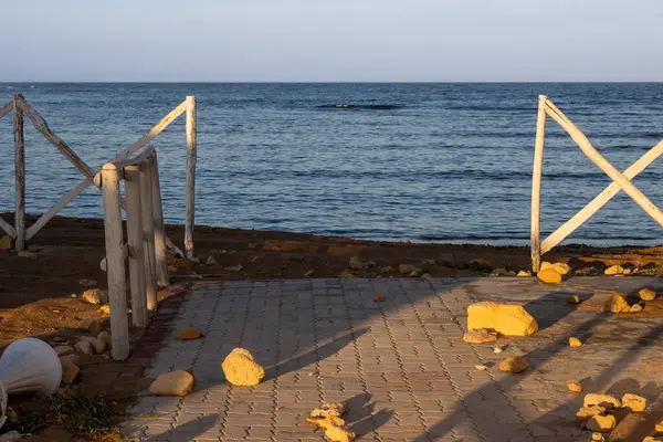 Akdeniz 'in sakin suları. Beyaz ahşap çitler, sabah güneşiyle boyanmış altın rengine boyanmış, taşlarla birlikte. Spiaggia Sibilliana, Marsala, Batı Sicilya, İtalya.