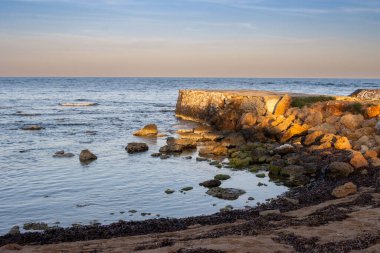 Akdeniz 'in sakin mavi suları. Sahilin kayalık kısmının kıvrımları. Güneş doğarken turuncu ve mavi gökyüzü. Koyu mavi bulutlar. Spiaggia Sibiliana, Marsala, Sicilya, İtalya.