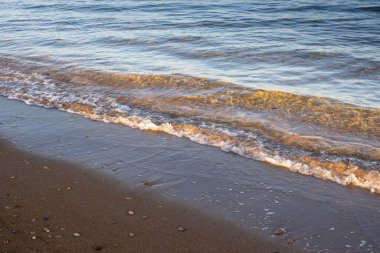 Küçük çakıl taşlarıyla kumlu kumsalın çapraz bileşimi ve küçük gel-git dalgalarıyla Akdeniz 'in şeffaf suyu. Sabah güneşi. Spiaggia Sibiliana, Petrosino, Marsala, Sicilya, İtalya.