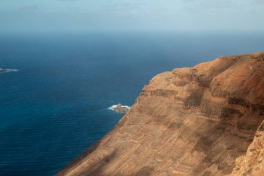 Adanın kuzeyindeki yüksek kayalıklar Atlantik Okyanusu 'nda. Beyaz bulutlu mavi gökyüzü. Lanzarote, Kanarya Adaları, İspanya.