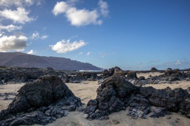 Adanın kuzeydoğusundaki plajda lav kayaları, beyaz kum ve Atlantik Okyanusu 'nun sığ suları var. Beyaz bulutlu mavi gökyüzü. Playa de Caleton Blanco, Lanzarote, Kanarya Adaları, İspanya.