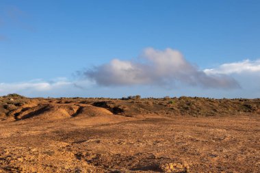 Kumlu toprağın turuncu rengi, çakıl ve daha büyük taşlarla dolu. Altın saatle renklendirilmiş. Kuru ve ıssız topraklar. Lanzarote, Kanarya Adaları, İspanya.