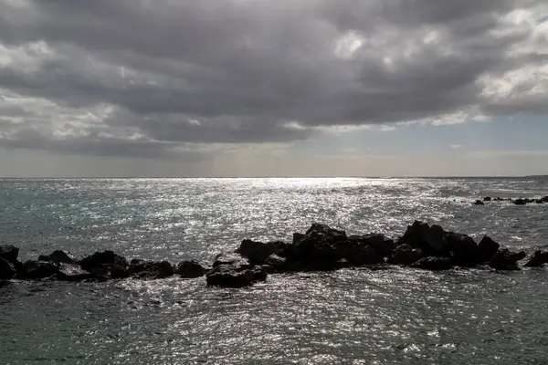 Atlantik Okyanusu kıyısındaki volkanik kayalar. Kışın bulutlu bir gökyüzü. Arrieta, Lanzarote, Kanarya Adaları, İspanya.