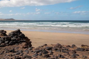Atlantik Okyanusu kıyısındaki volkanik kayalar. Beyaz kumlu bir sahil. Kışın bulutlu bir gökyüzü. Famara, Lanzarote, Kanarya Adaları, İspanya.