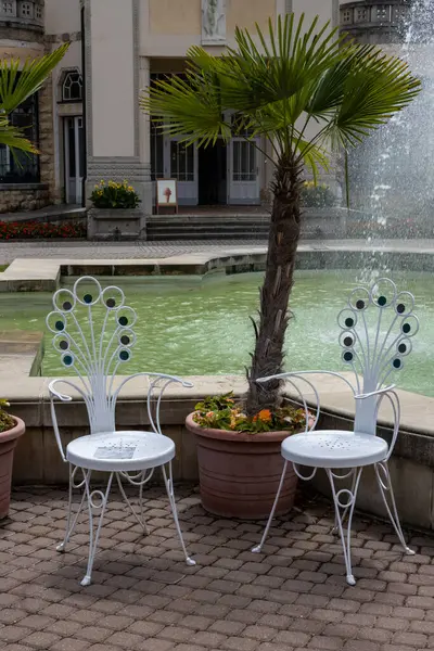 stock image Pool infront of historical spa hotel on the Spa Island. Two ornate chairs for taking selfies. Palm tree and a fountain. Piestany, Slovakia.