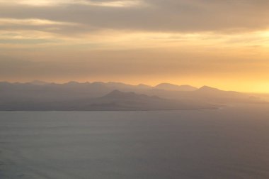 Atlantik okyanusunun sakin suları. Kışın bulutlu bir gökyüzü. Renkli bulutlarla gün batımı. Bakış açısı Miarador del Rio, Lanzarote, Kanarya Adaları, İspanya.