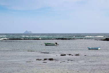 Beyaz kumlu ve sığ sulu bir sahil. Siyah volkanik küçük kayalar. Kışın hafif bulutlu mavi gökyüzü. Caleton Blanco, Lanzarote, Kanarya Adaları, İspanya.