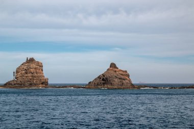 Adanın kuzeyindeki kayalıklardan ve volkanik kayalıklardan bir tekne görüntüsü. Kışın beyaz bulutlu mavi gökyüzü. Mirador del Rio, Lanzarote, Kanarya Adaları, İspanya.