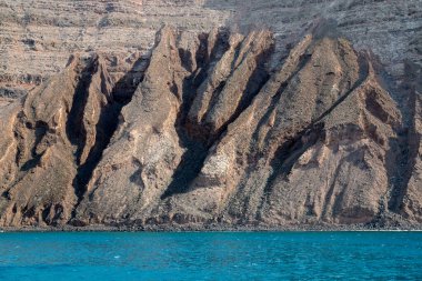 Adanın kuzeyindeki kayalıklardan ve volkanik kayalıklardan bir tekne görüntüsü. Kışın beyaz bulutlu mavi gökyüzü. Mirador del Rio, Lanzarote, Kanarya Adaları, İspanya.