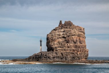 Adanın kuzeyindeki kayalıklardan ve volkanik kayalıklardan bir tekne görüntüsü. Kışın beyaz bulutlu mavi gökyüzü. Mirador del Rio, Lanzarote, Kanarya Adaları, İspanya.