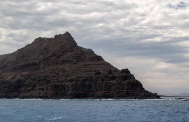Adanın kuzeyindeki kayalıklardan ve volkanik kayalıklardan bir tekne görüntüsü. Kışın beyaz bulutlu mavi gökyüzü. Mirador del Rio, Lanzarote, Kanarya Adaları, İspanya.