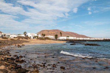 Atlantik okyanusunun sakin suları ve tipik beyaz bir mimari. Arka plandaki dağ. Kışın beyaz bulutlu mavi gökyüzü. Caleta del Sebo, La Graciosa, Kanarya Adaları, İspanya.