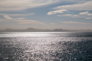 Lanzarote 'nin kuzeyindeki dağlar sisli. Atlantik okyanusunun sakin suları. Kışın bulutlu bir gökyüzü. Caleta del Sebo, La Graciosa, Kanarya Adaları, İspanya.