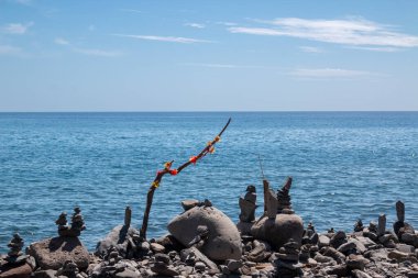 Plaj çakıllarından yapılmış taş kuleler. Atlantik Okyanusu kıyısında. Beyaz bulutlu mavi gökyüzü. Madalena do Mar, Madeira, Portekiz.
