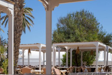 Gün boyunca boş sandalyeler ve masalarla dolu bir teras. Bir tatil köyünün restoranının bir parçası. Güzel taze yeşillik. Djerba, Tunus, Afrika.