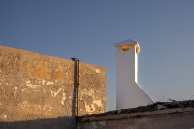 Beyaz bacalı bir çatı katı. Altın saatin atmosferi, aydınlanmış ve eski yapılandırılmış bir duvar. Parlak mavi gökyüzü. Djerba, Tunus, Afrika.