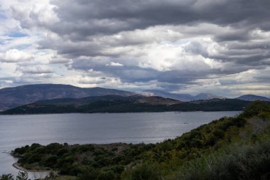 İyonik denizin sakin suları. Arnavutluk 'un dağlarındaki Yunan adasından görüntü. Yazın sonunda yoğun bulutlarla dolu bir gökyüzü. Kuzey Doğu Korfu, Yunanistan.