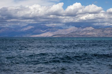 Adanın kuzeydoğusundaki İyon Denizi 'nin mavi suları. Arnavutluk 'taki dağlar ufukta görünüyor. Beyaz bulutlu mavi gökyüzü. Agios Spyridon, Korfu, Yunanistan.