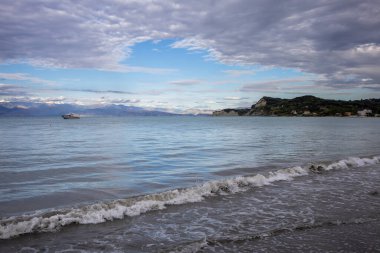 Calm water of the Ionic sea, with a boat. Mountains in Albania on the horizon. Intense clouds on the sky. Sidari, Corfu, Greece. clipart