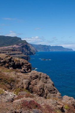 Baharın güneşli bir gününde, Atlantik ve yarımadanın kayalıkları. Beyaz bulutlu mavi gökyüzü. Vulcao Penha de Aquia, Madeira, Portekiz.