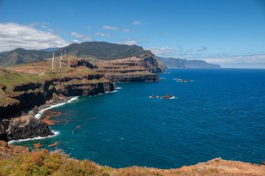 Baharın güneşli bir gününde, Atlantik ve yarımadanın kayalıkları. Beyaz bulutlu mavi gökyüzü. Vulcao Penha de Aquia, Madeira, Portekiz.