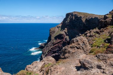 Baharın güneşli bir gününde, Atlantik ve yarımadanın kayalıkları. Beyaz bulutlu mavi gökyüzü. Vulcao Penha de Aquia, Madeira, Portekiz.