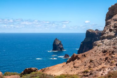 Baharın güneşli bir gününde, Atlantik ve yarımadanın kayalıkları. Beyaz bulutlu mavi gökyüzü. Vulcao Penha de Aquia, Madeira, Portekiz.