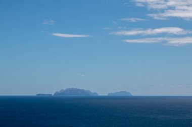 Atlantik okyanusunun sakin suları. Ufukta Madeira 'ya ait küçük adalar var. Beyaz bulutlu mavi gökyüzü. Görüntü: Vulcao Penha de Aquia, Madeira, Portekiz.
